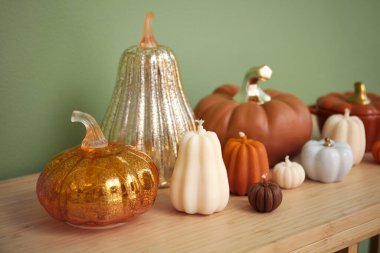 Yeşil duvarın yanında balkabağı şeklinde mumlar ve dekor olan raf ünitesi.