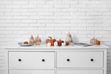 Beyaz tuğla duvarın yanında balkabağı, dekor ve şarjör şeklinde mumlarla dolu çekmeceler.