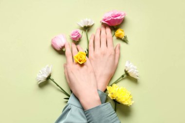 Açık yeşil arka planda farklı taze çiçekleri olan kadın elleri. Bakım kavramı