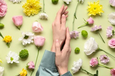 Açık yeşil arka planda farklı taze çiçekleri olan kadın elleri. Bakım kavramı