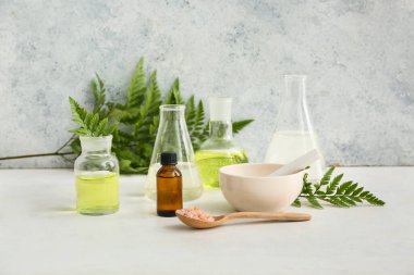 Bir şişe yağ, numune ve doğal kozmetik malzemeleriyle dolu laboratuvar bardakları grunge duvarının yanındaki beyaz masada.