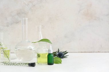 Şişeler dolusu ürün, numune ve malzemelerle dolu laboratuvar bardakları ve doğal kozmetik malzemeleri grunge duvarının yanındaki beyaz masada hazırlamak için.