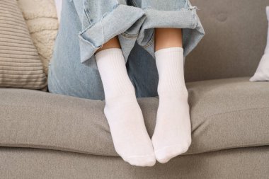 Beyaz çoraplı bir kadın evdeki kanepede oturuyor.