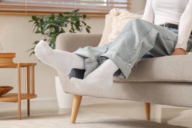 Beyaz çoraplı kadın evdeki kanepede oturuyor.