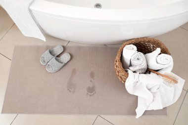 Yerde ıslak ayak izleri, terlikler ve havlular olan banyo paspası.