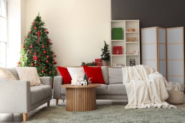 Oturma odasının içinde kanepeler, Noel ağaçları ve mum tutacakları var.