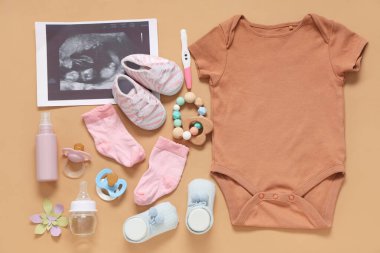 Bebek kıyafetleri, ultrason görüntüsü, hamilelik testi ve bej arka planda meme uçları olan kompozisyon