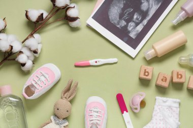 Ayakkabıdan yapılmış çerçeve, sonogram görüntüsü, hamilelik testleri ve yeşil arka planda bulunan kozmetik ürünleri şişeleri