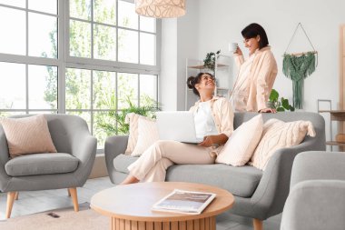 Evdeki kanepede dizüstü bilgisayar kullanan genç lezbiyen çift.