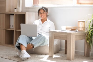 Genç Afro-Amerikalı soru cevap mühendisi dizüstü bilgisayarlı evde armut koltukta oturuyor.