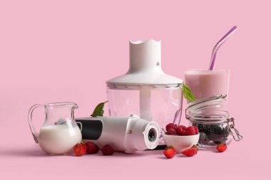 Modern blender, bir bardak smoothie ve pembe arka planda böğürtlen.