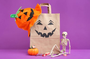 Mor arka planda Cadılar Bayramı için kağıt alışveriş torbası, süsleme ve tatlı kompozisyonu