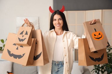 Şeytan boynuzlu genç bir kadın Cadılar Bayramı 'nda evde alışveriş torbalarıyla dolaşıyor.