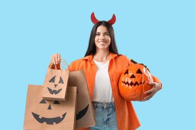 Cadılar Bayramı balkabağı ve mavi arka planda alışveriş torbalarıyla şeytan boynuzlu genç bir kadın.