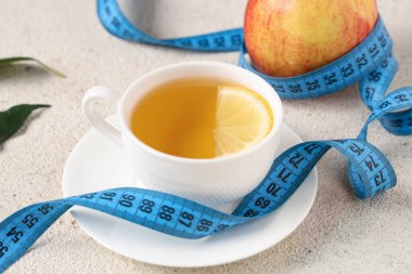 Bir fincan diyet çayı, ölçü bandı ve arka planda elma. Kilo verme konsepti