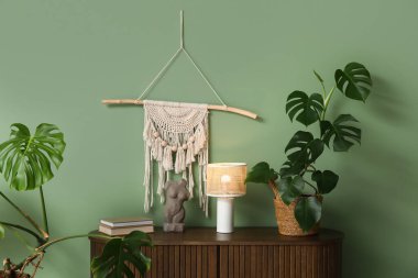 Parlayan lambalı çekmeceler, Monstera bitkisi, insan figürü ve yeşil duvarın yakınındaki kitaplar.