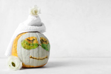 Çizilmiş yüzlü balkabağı, kil maske, havlu, göz altı bantları ve beyaz arka planda çiçekler