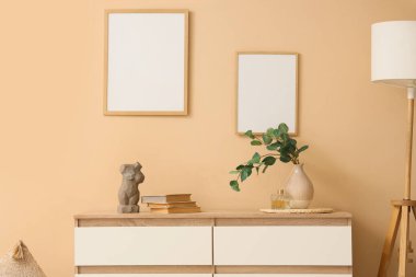 Vazoda dalları olan çekmeceler, bej duvarda kitaplar ve çerçeveler.