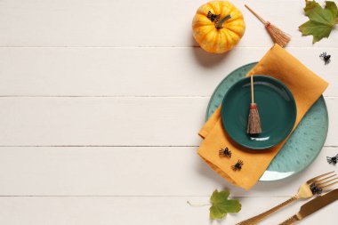 Beyaz ahşap arka planda süpürgeler, örümcekler ve balkabağıyla Cadılar Bayramı kutlaması için şenlik masası.