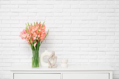 Beyaz tuğla duvarın yanında, klozette gladiolus çiçekleri ve heykelciği olan vazo.