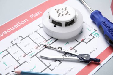 Tahliye planına sahip modern duman dedektörü, tornavida ve gri arka planda bir çift pusula, yakın plan