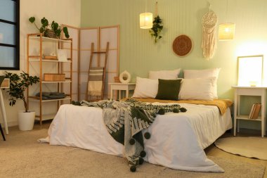 Kareli rahat bir yatak, raf ünitesi, komodinlerin yanında parlayan lambalar.