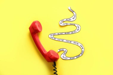 Phone receiver and paper tape with words BLAH on yellow background. Gossip concept clipart