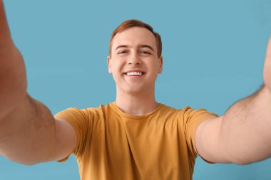 Genç adam mavi arka planda selfie çekiyor, yakın plan.