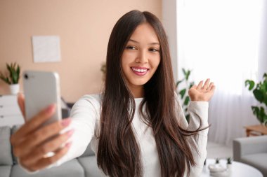 Cep telefonlu genç Asyalı kadın evde selfie çekiyor.