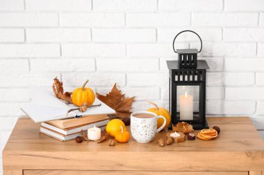 Bir kupa lezzetli yeşil çay, balkabağı, mum ve meşe palamudu beyaz tuğla duvarın yanındaki çekmecede.