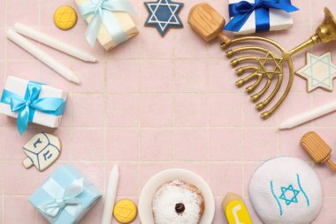 Menorah 'tan yapılmış çerçeve, mumlar, donut ve pembe fayanslı arka planda hediye kutuları. Hanuka kutlaması