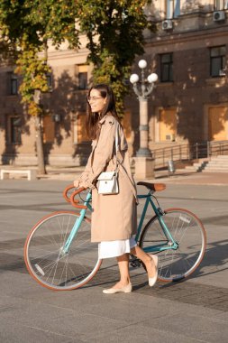 Şehir caddesinde bisikleti olan güzel genç bir kadın.