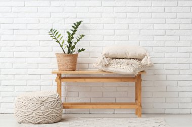 Yastıklı bank, ev bitkisi ve beyaz tuğla duvarın yanındaki oda.