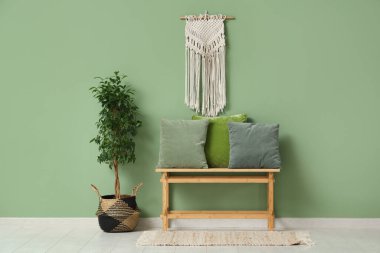 Dekoratif ağaç ve yeşil duvarın yanındaki minderli bankta.