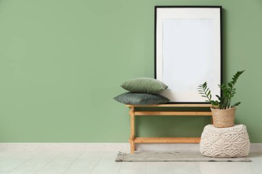 Odada yeşil duvarın yanında bir tezgah, yastıklar ve çerçeve