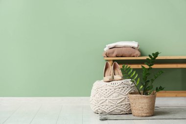 Yeşil duvarın yanındaki bankta çiçek, kıyafet, puf ve ayakkabılar var.