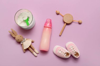 Beslenme şişesi, bebek sütü formülü, leylak arka planda oyuncaklar ve popolar
