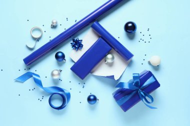 İçinde ambalaj malzemeleri ve mavi arka planda farklı dekorasyonlar olan Noel hediyesi kutuları.