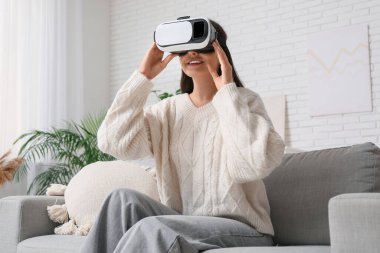 Evdeki kanepede VR gözlük takan genç bir kadın.