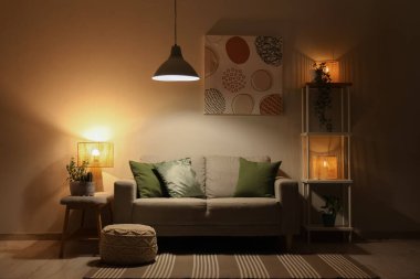 Konforlu kanepe, raf ünitesi ve oturma odasının içinde parlayan lambalar olan bank.