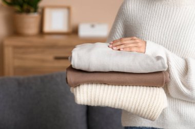 Evde kalın süveter yığını olan genç bir kadın, yakın plan.