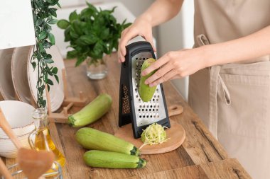 Genç bir kadın mutfakta taze kabak rendeliyor.