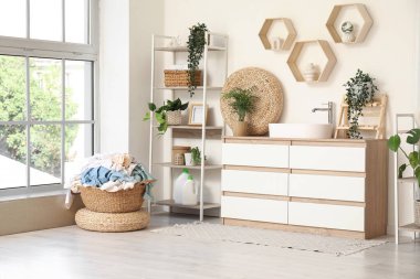 Çamaşır sepetli, şifoniyerli ve çiçekli çamaşırhanenin içi.