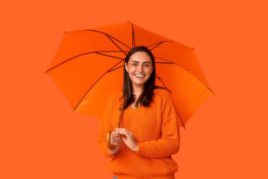 Turuncu arka planda şemsiyesi olan mutlu genç bir kadın.