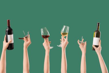 Yeşil arka planda tirbuşon, şişe ve şarap bardakları tutan kadın elleri