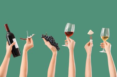 Yeşil arka planda şarap, peynir, üzüm ve tirbuşon tutan kadın eller.