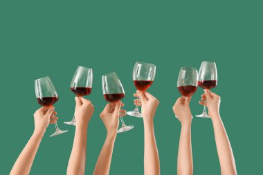 Yeşil arka planda kırmızı şarap kadehlerini tutan kadın eller.