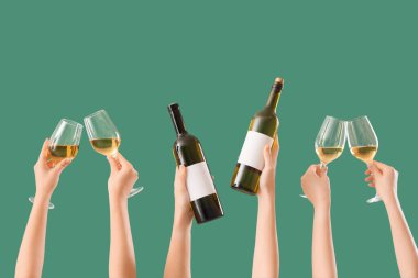 Yeşil arka planda şişeleri ve şarap kadehlerini tutan kadın eller