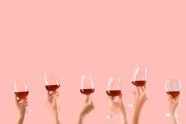 Pembe arka planda kırmızı şarap kadehleri tutan kadın eller.