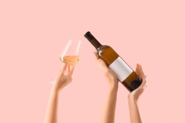 Kadın elleri pembe arka planda şişe ve şarap tutuyor.